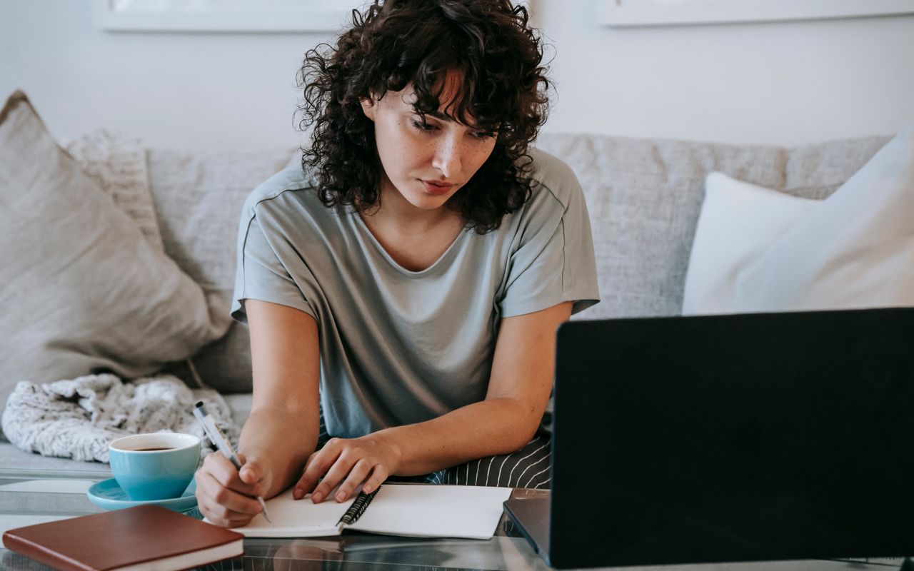 Pessoa estudando em casa com computador e caderno
