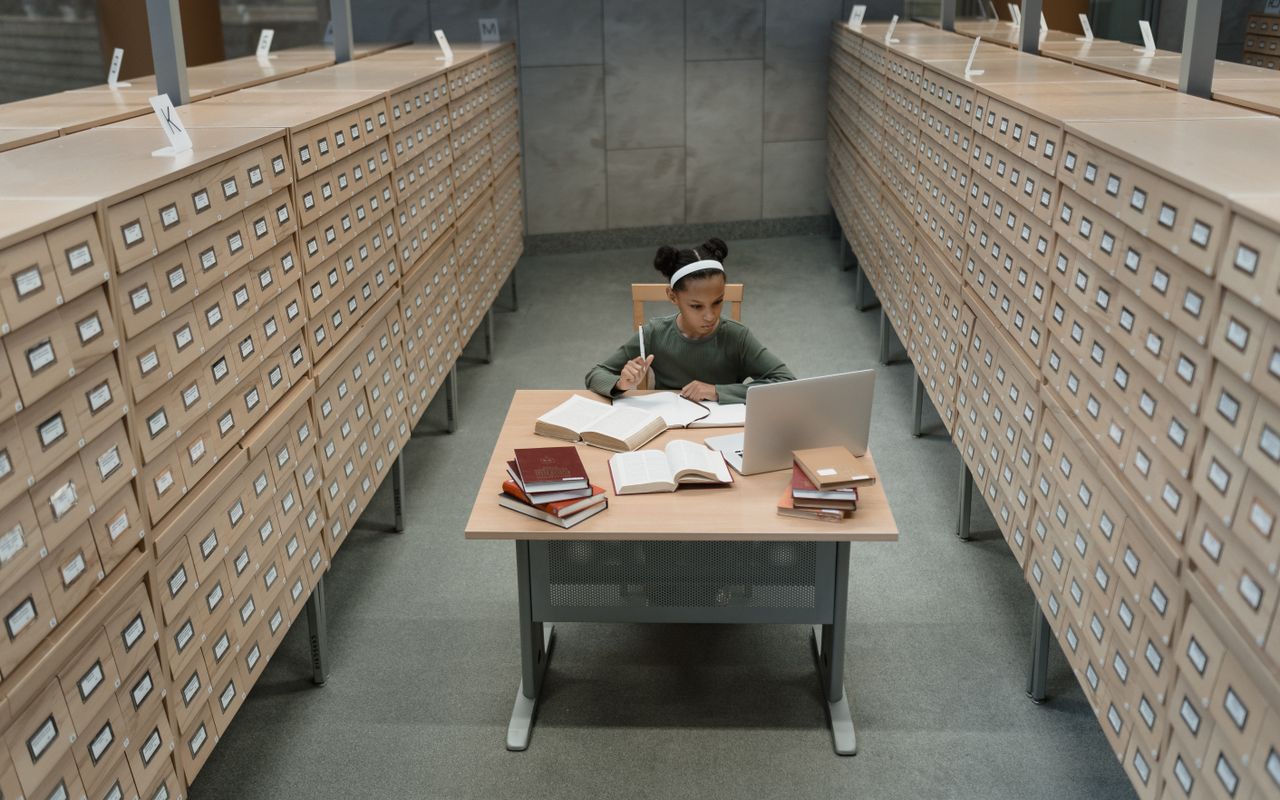 Estudante pesquisando com computador e livros em uma biblioteca histórica